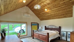 Un dormitorio con techo de madera, una cama, una mesa de comedor y vista a un coche a través de una ventana.