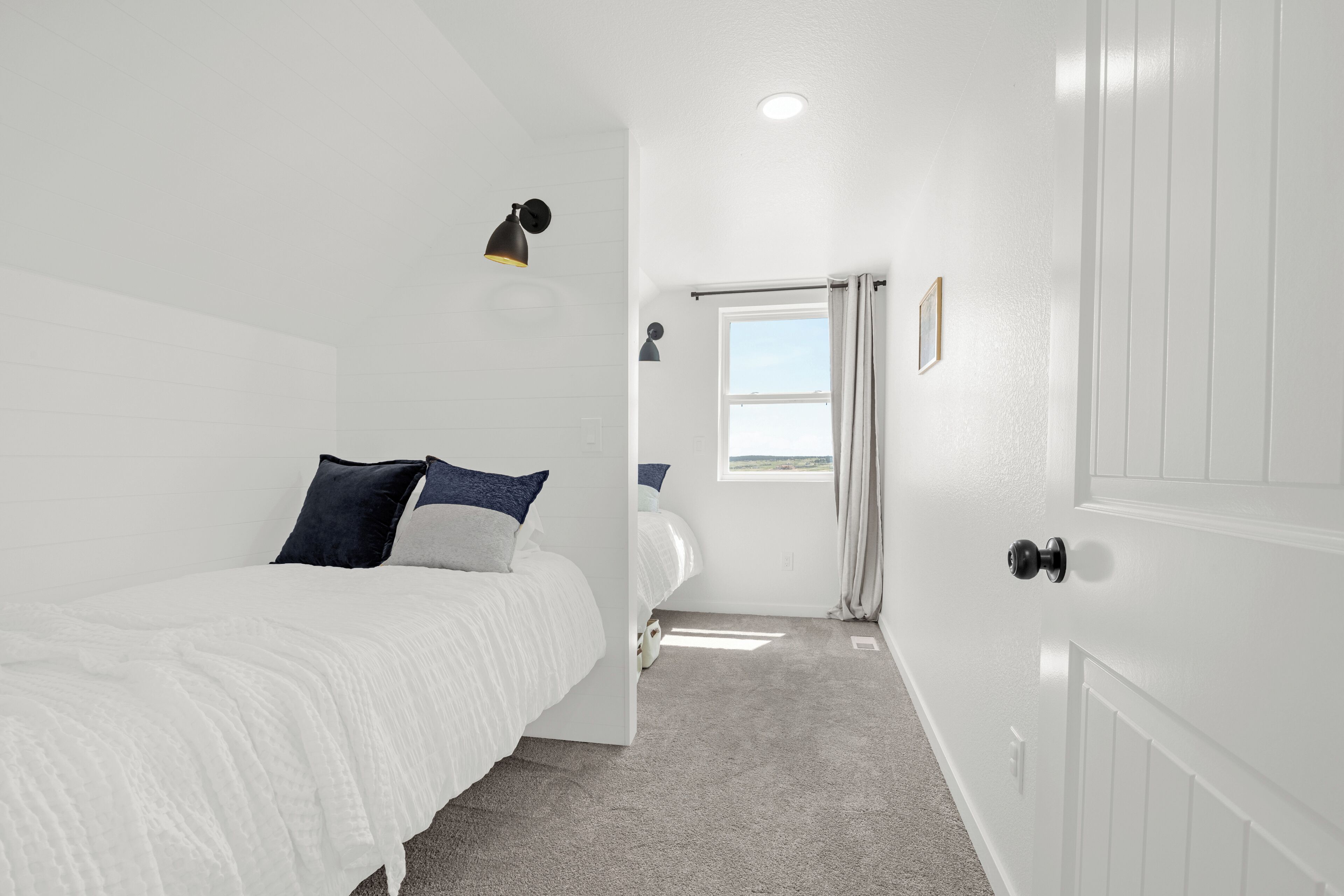 Ein Schlafzimmer mit Bett, Nachttischlampe, einem Fenster mit Vorhängen und einer Tür.