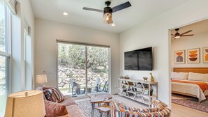 A spacious living room with a large window, a sofa, a coffee table, and a TV mounted on the wall. - Walk to Southern Utah Campus: Home w/ Fire Pit (Cedar City)