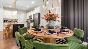 A modern kitchen with white cabinets, a central island, and a dining area with green upholstered chairs and a round wooden table.