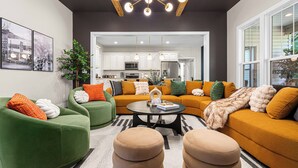 A modern living room with green and orange sofas, a coffee table, and a kitchen in the background.