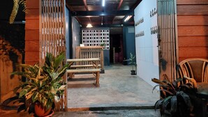 The entrance of Baaan Hostel with wooden walls, a signboard, and a few potted plants.