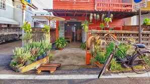 A red building with a covered porch, potted plants, and a bicycle.