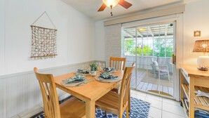 Comedor con una mesa de madera dispuesta para cuatro, un ventilador de techo y vistas a un patio exterior a través de un ventanal.