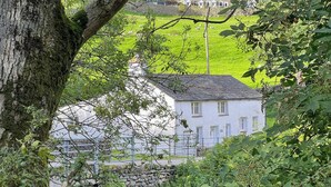 A white building with a stone wall in front, surrounded by greenery.