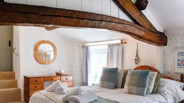 A bedroom with a large bed, a wooden dresser, a round mirror, and a window with curtains.