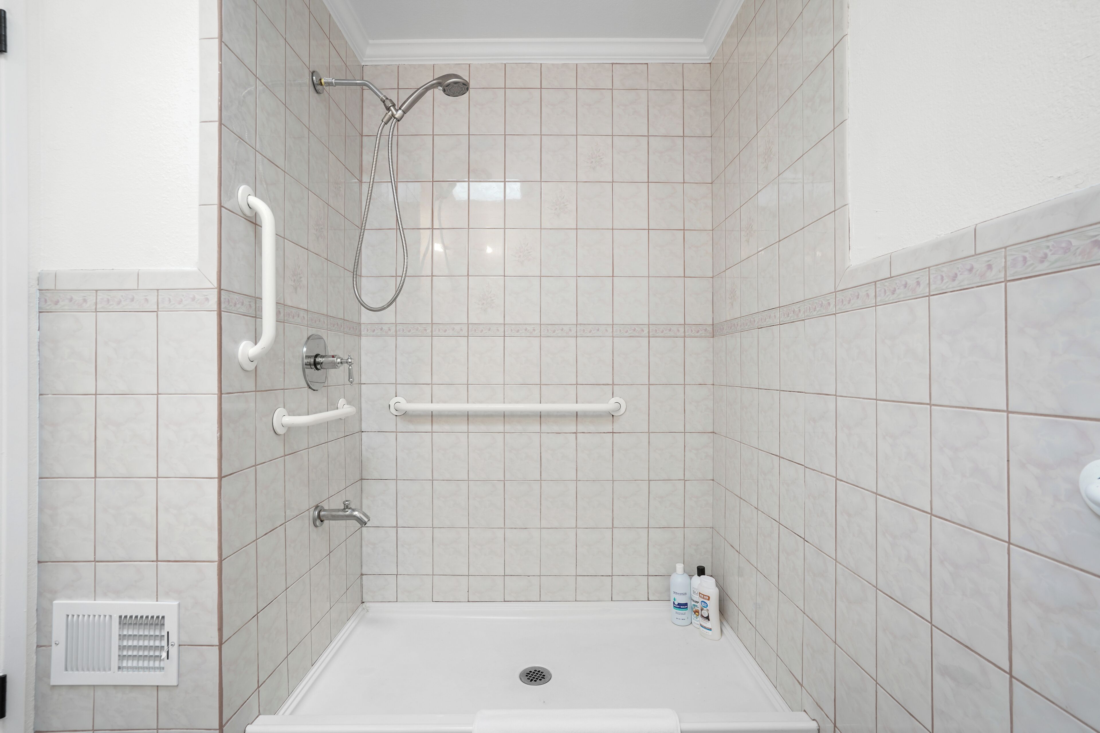 A bathroom with a shower, grab bars, and a hand dryer.