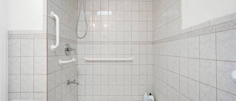 A bathroom with a shower, grab bars, and a hand dryer.