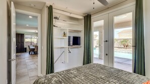 A bedroom with a bed, a ceiling fan, a TV mounted on a wall, and a sliding glass door leading to a pool area. - Pet-Friendly LHC Home w/ Temp-Controlled Pool! (Lake Havasu City)