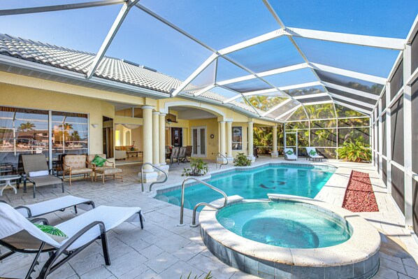A covered outdoor swimming pool with lounge chairs and a hot tub, surrounded by a glass enclosure. - Pool, Spa & Dock: Waterfront Tarpon Point Home (Cape Coral)