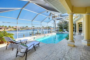 An indoor swimming pool with clear views of the water, surrounded by lounge chairs and a covered patio area. - Pool, Spa & Dock: Waterfront Tarpon Point Home (Cape Coral)