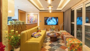 A modern living room with a sofa, ottoman, and a coffee table. There is a TV mounted on the wall and a window with curtains. - Premium 1BR family friendly condo with full balcony views in BGC (Taguig City)