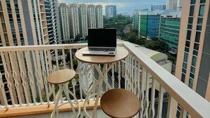 A balcony with a laptop on a small table, two chairs, and a view of high-rise buildings. - Premium 1BR family friendly condo with full balcony views in BGC (Taguig City)