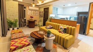 A modern living room with a sofa, ottomans, and a coffee table. There is a kitchen area visible in the background. - Premium 1BR family friendly condo with full balcony views in BGC (Taguig City)