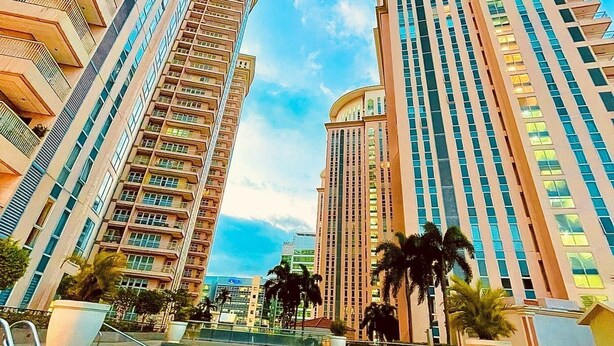 A modern hotel with a swimming pool, high-rise buildings, and palm trees. - Premium 1BR family friendly condo with full balcony views in BGC (Taguig City)