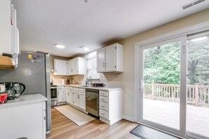 A modern kitchen with white cabinets, a stainless steel refrigerator, and a dishwasher. There is a large sliding glass door leading to a wooden deck. - 3 Mi to Dtwn Cary: Family Home w/ Deck! (Cary)