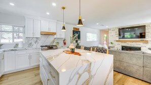 A modern kitchen with white cabinetry, a large marble island, pendant lighting, and a built-in TV. - Walk to The Village Shops/Eats: Big Bear Lake Home (Big Bear Lake)