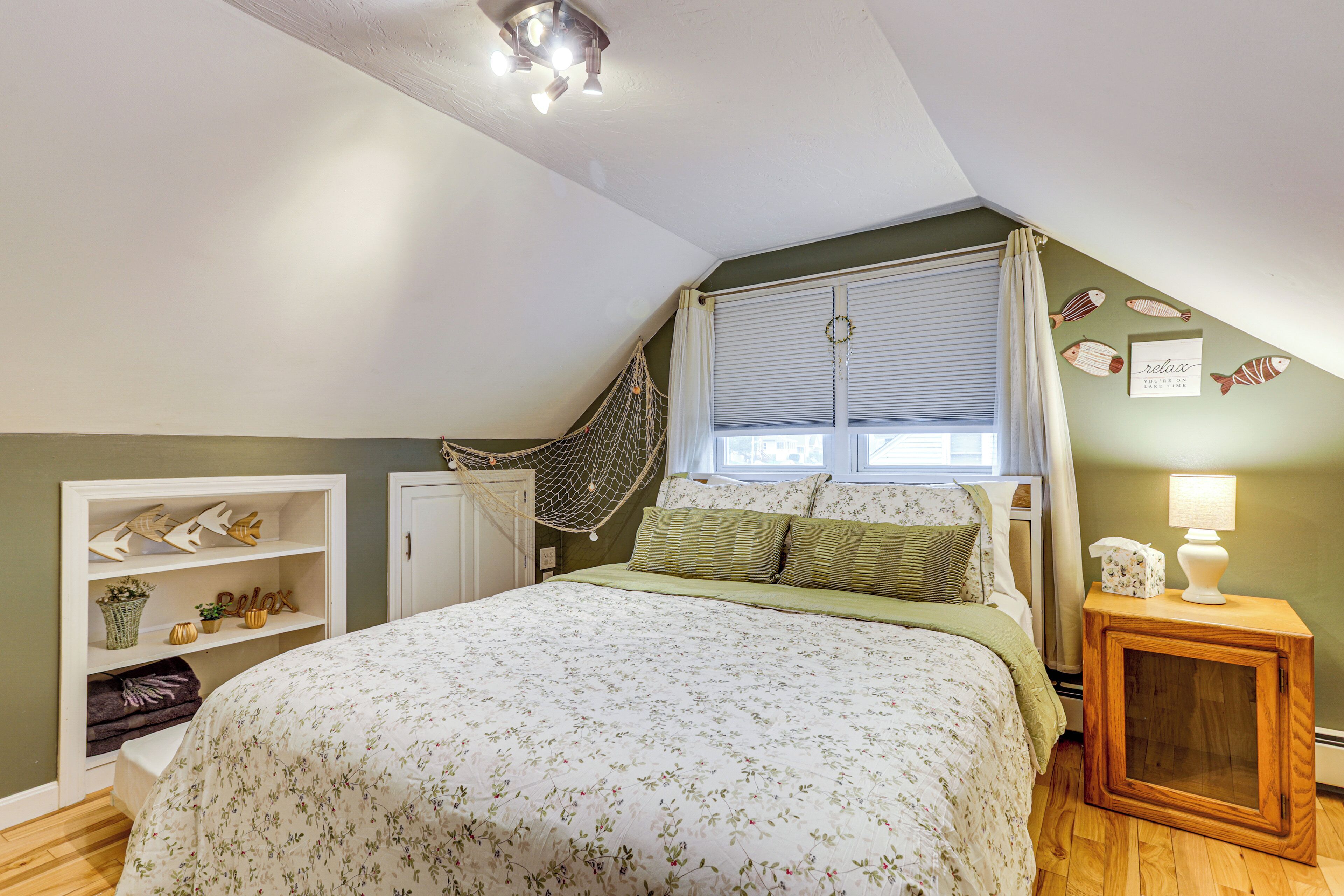A bedroom with a bed, a window with curtains, a hammock, a bedside table with a lamp, and a wall with fish decorations.