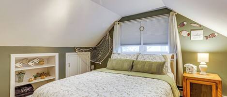A bedroom with a bed, a window with curtains, a hammock, a bedside table with a lamp, and a wall with fish decorations.