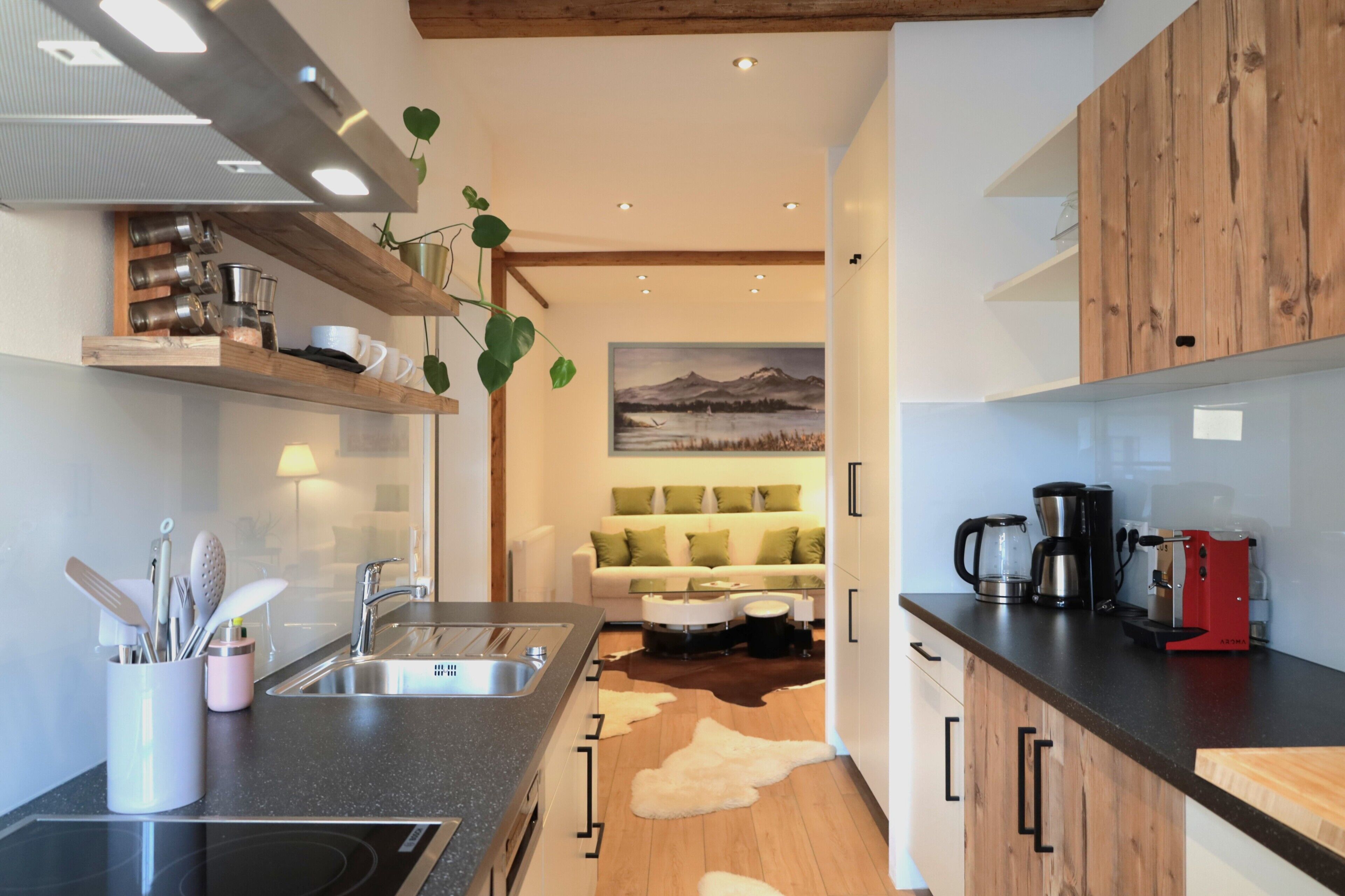 A modern kitchen with a wooden countertop, stainless steel sink, and a dining area with a sofa and a painting of mountains.