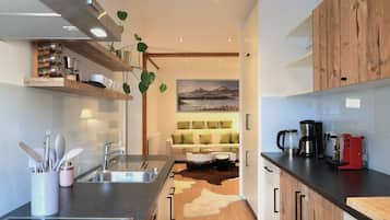 A modern kitchen with a wooden countertop, stainless steel sink, and a dining area with a sofa and a painting of mountains.