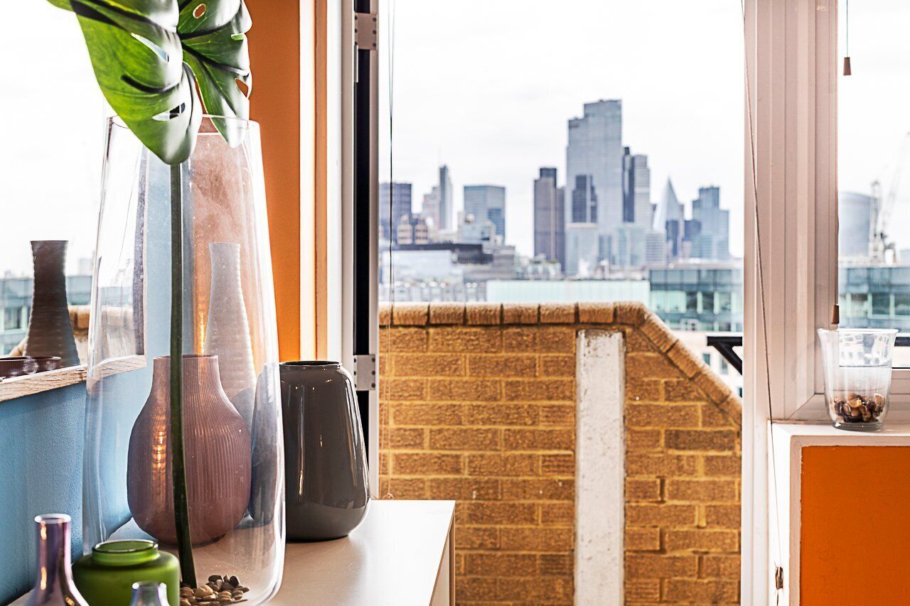 A view of a city skyline from a window with a brick wall and a table with vases.