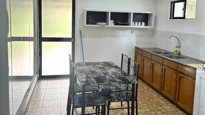Una cocina con piso de baldosas, una mesa de comedor con sillas, gabinetes de madera, un ventanal y un ventilador de techo.