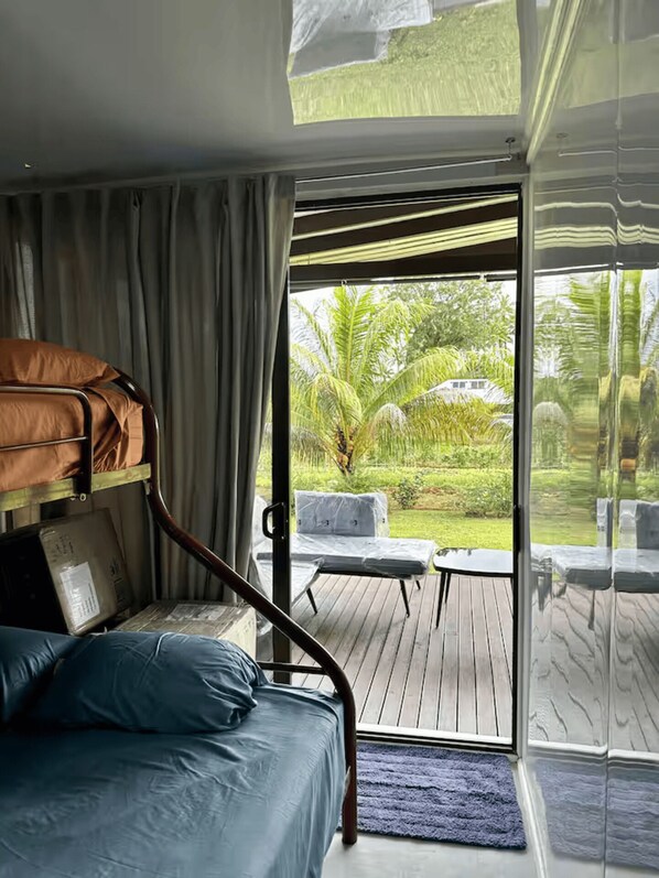 A room with a bunk bed, a small table, and a view of a garden through a glass door. - Furnished Modern Farm Flat Tuvurara Savusavu (Nakasa)