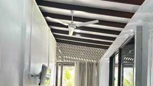 Una habitación con ventilador de techo, televisor montado en la pared, una mesita pequeña y un sofá.