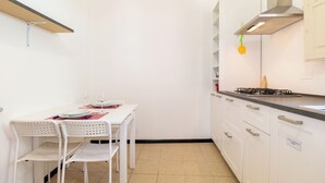 Une petite cuisine avec des meubles blancs, une cuisinière à gaz et une table à manger avec des chaises.