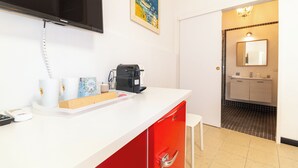 Une chambre d’hôtel avec un comptoir blanc et rouge, une machine à café, un téléphone et un tableau accroché au mur.