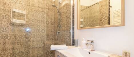 Un baño con azulejos decorativos, una ducha, un lavabo con artículos de aseo y un espejo.
