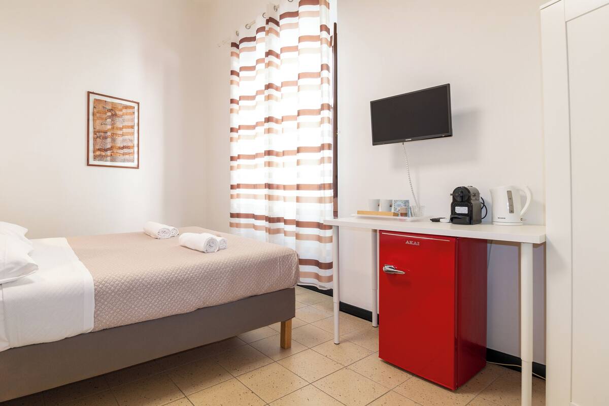 Une chambre d’hôtel avec un lit, un bureau doté d’un meuble rouge, une télévision et un rideau de douche.