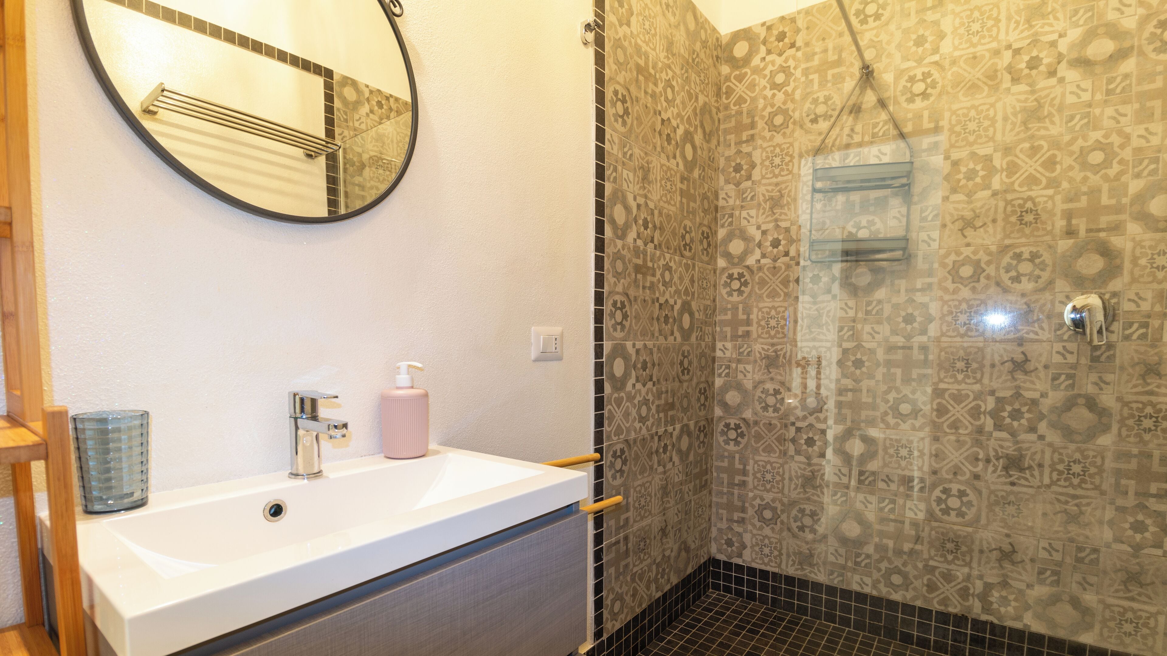 A bathroom with a white sink, a mirror, a shower with patterned tiles, and a hand dryer.