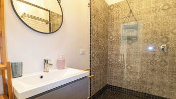 A bathroom with a white sink, a mirror, a shower with patterned tiles, and a hand dryer.