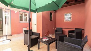 Un espace patio aménagé avec des meubles en osier, une table et un parasol vert.