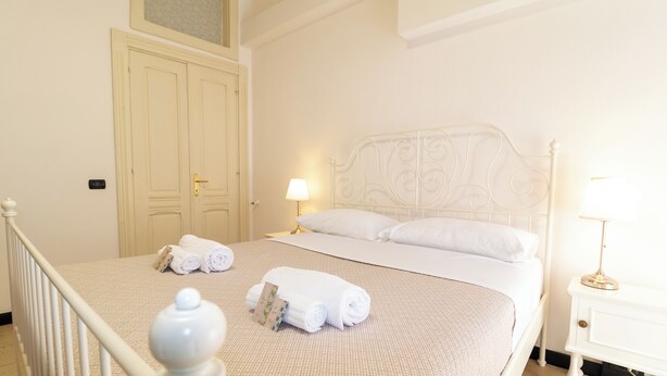 Un lit bien fait, avec du linge de lit blanc, une table de chevet avec une lampe et une porte dotée d’une poignée en laiton.