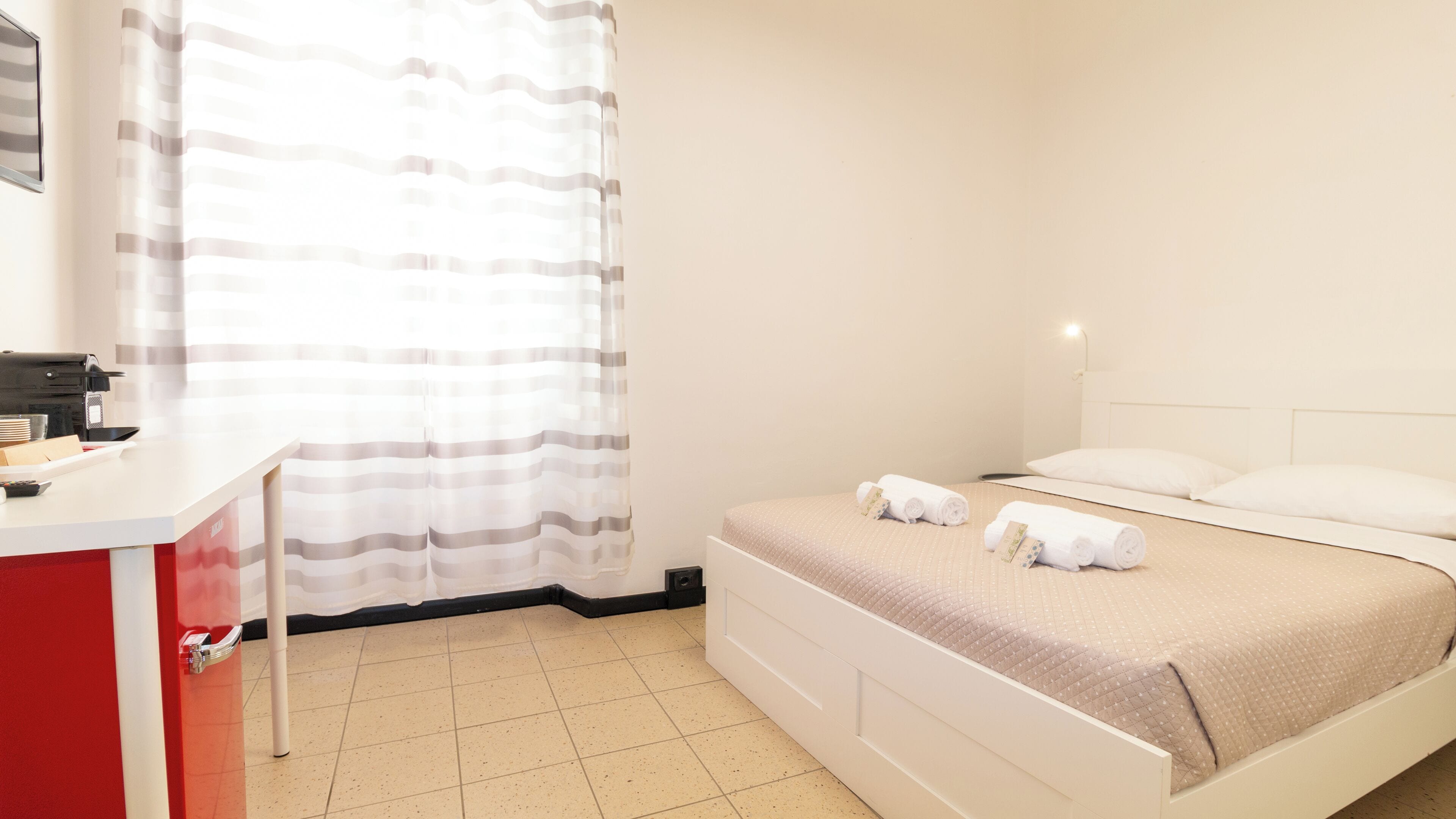 Ein Hotelzimmer mit Bett, Schreibtisch mit Computer und Fenster mit Vorhängen.