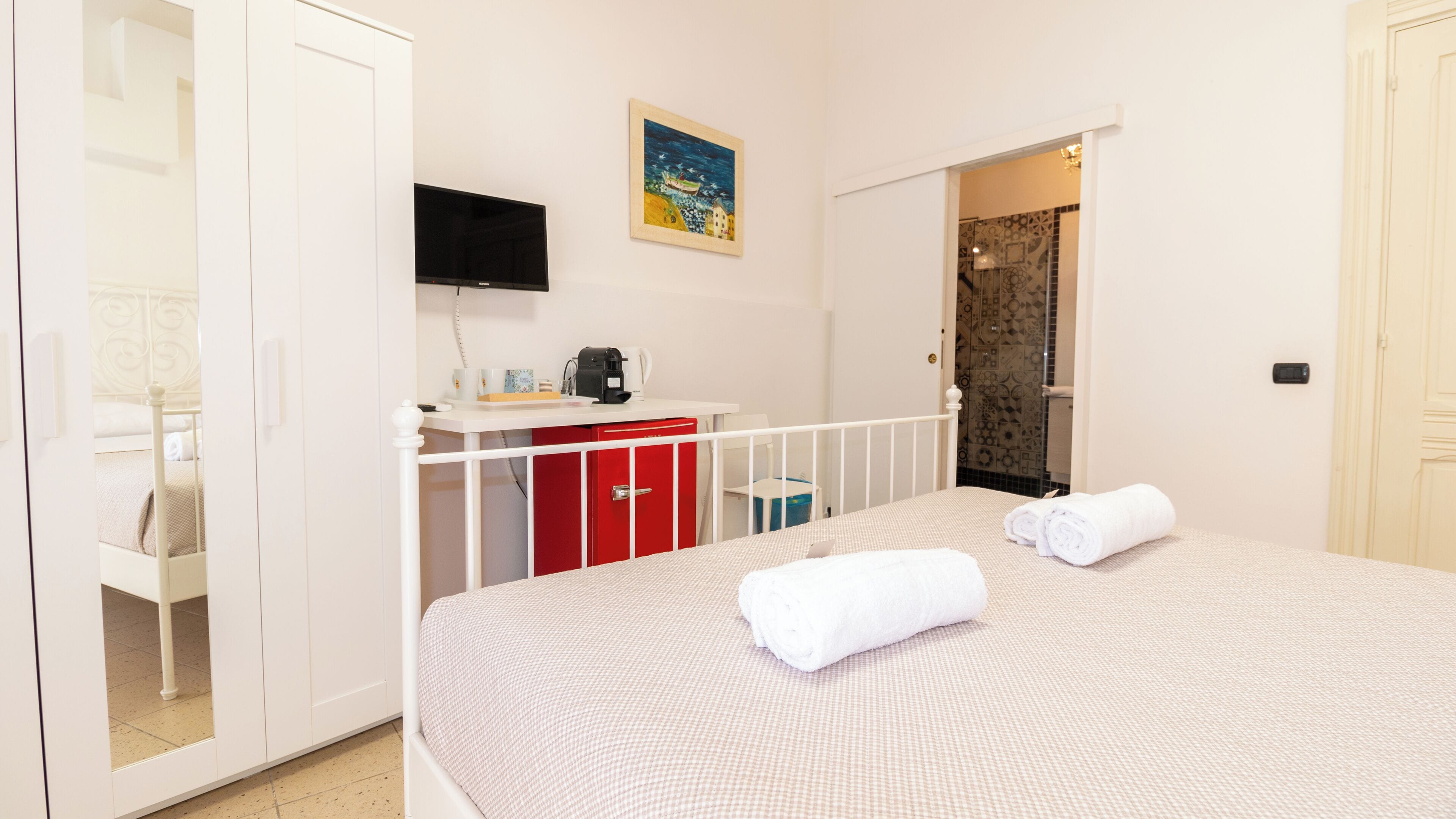 Een hotelkamer met een bed, een bureau met een rode kast, een televisie en een schilderij aan de muur.