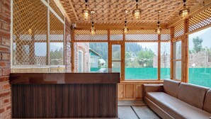 A wooden interior with a bench and a cushioned seating area, large windows, and a patterned ceiling. - Bombay Residency (Pahalgam)