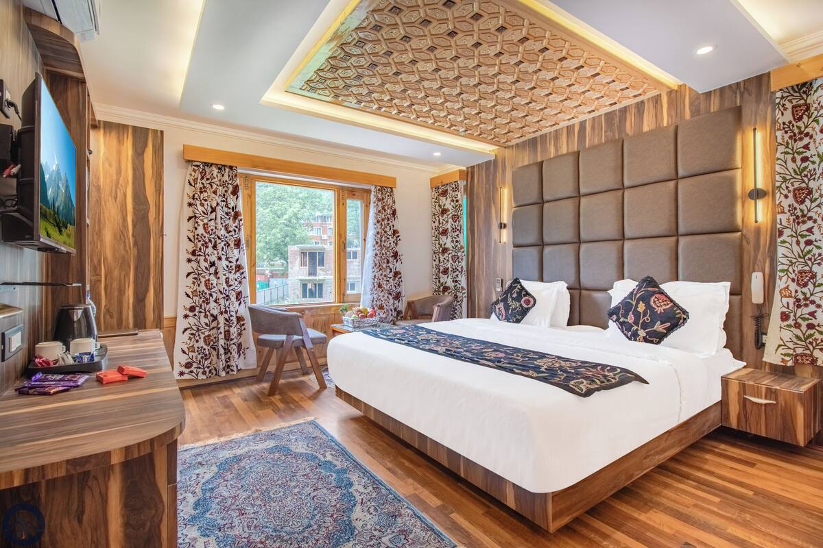 A bedroom with a large bed, a desk, a chair, a TV, and a view of the outside.