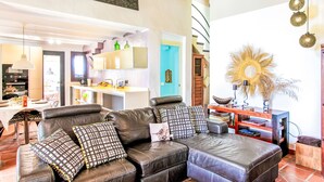 Ein modernes Wohnzimmer mit einer ledernen Eckcouch, einem Essbereich mit Tisch und Stühlen sowie einer Küche im Hintergrund.