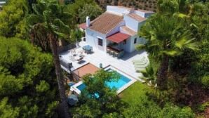 Eine Villa mit Schwimmbad, Sitzgelegenheiten im Freien und üppiger Bepflanzung.