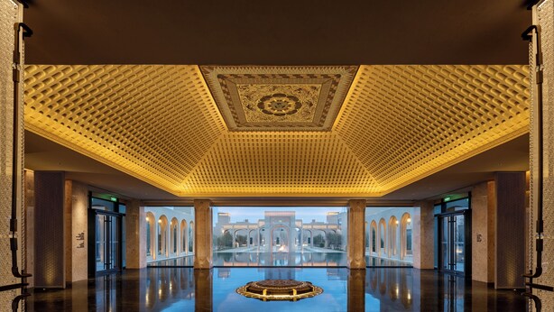 A spacious lobby with a reflective floor, a central decorative element, and a view of an outdoor courtyard with arches. - Wanda Vista Ganman Dunhuang (Jiuquan)