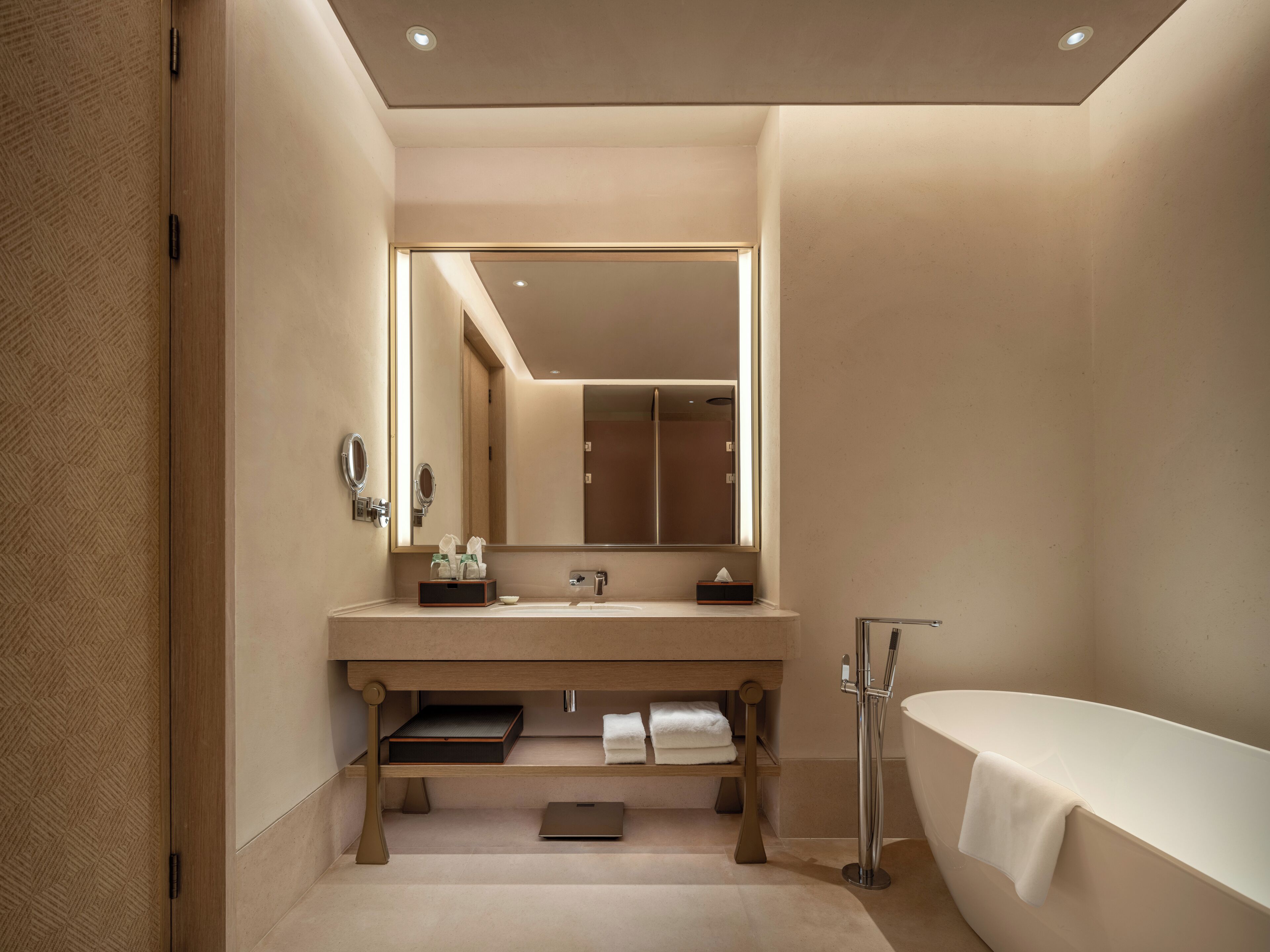 A modern bathroom with a large mirror, two sinks, a bathtub, and a vanity with storage.