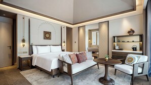 A modern hotel room with a large bed, a sofa, a round coffee table, and a small dining area. - Wanda Vista Ganman Dunhuang (Jiuquan)