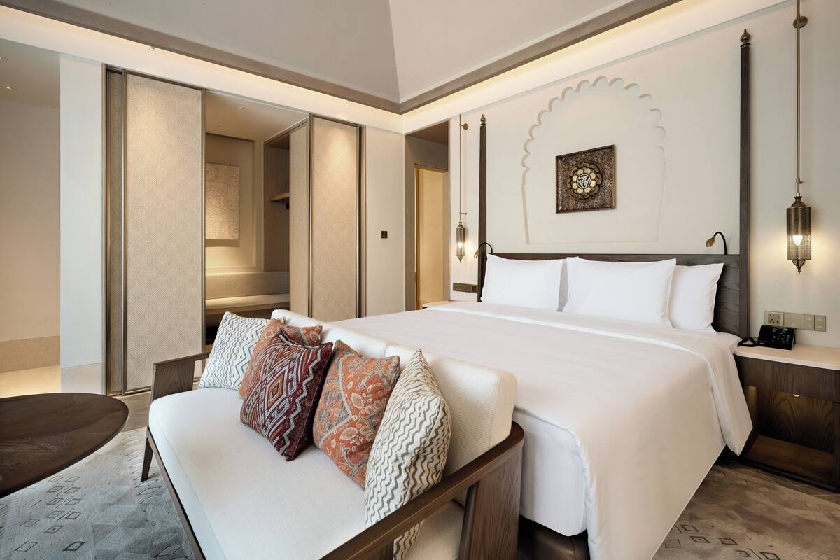 A hotel room with a large bed, a sofa, a bedside table, and a wall-mounted lamp.