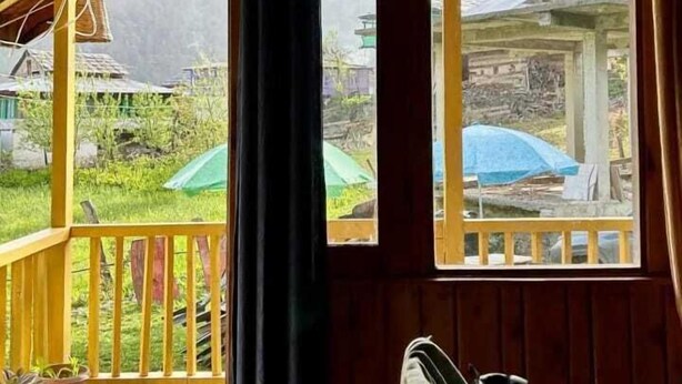En stuga byggd av trä med en veranda, stora fönster och utsikt över ett grönskande landskap.