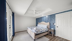 Une chambre à coucher avec un lit, une table de chevet, un ventilateur de plafond et une porte.