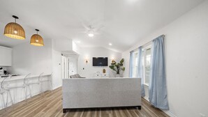 Une cuisine moderne dotée d’un îlot central, un coin repas avec des chaises transparentes et un espace de vie avec un canapé gris.